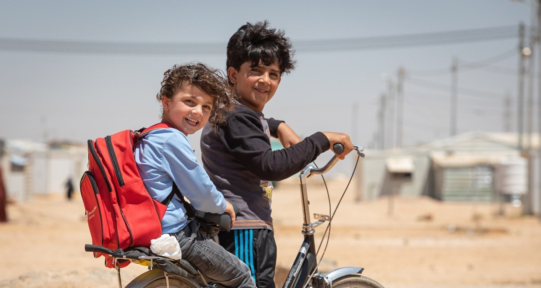 CH1363225 Bilal, 12, Takes His Brother Faisal, 5, To An Early Learning Centre On The Family Bicycle, In Za’Atari Camp For Syrian Refugees, Jordan