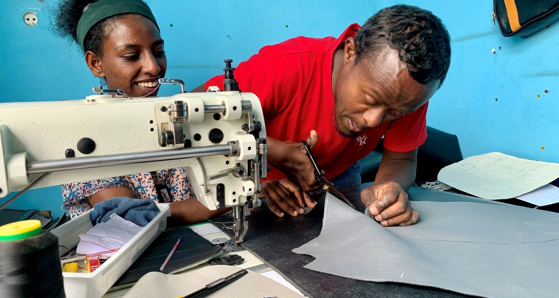 En ung kvinne og en mann sitter ved en symaskin og jobber.
