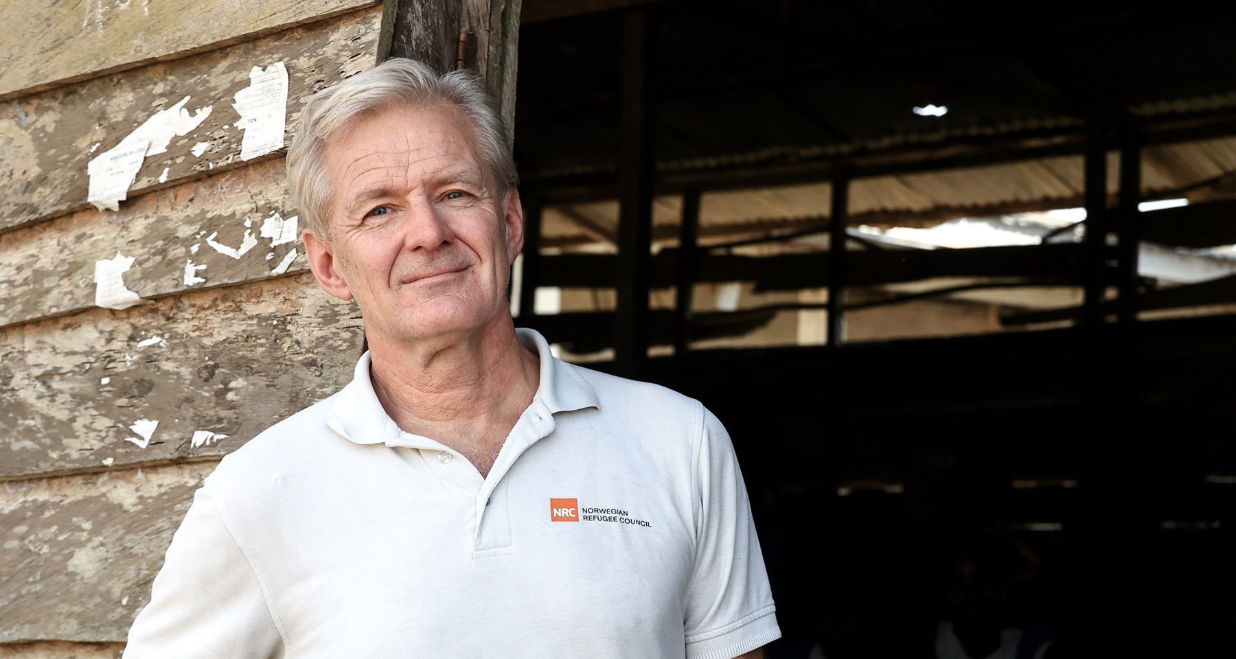 Jan Egeland står i hvit skjorte ved en slitt døråpning.