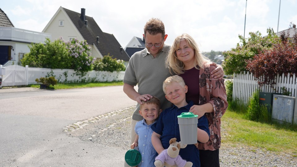 En familie med to voksne og to små gutter står i en gate med en bøsse i hånda. 