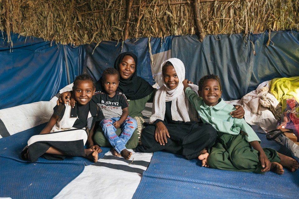 En mor og fire barn sitter i et telt og smiler.