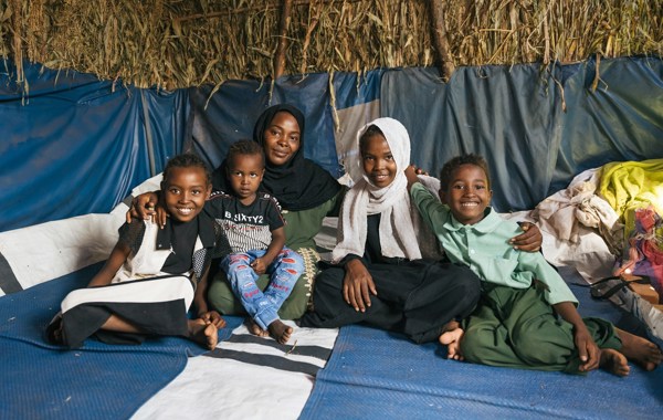 En mor og fire barn sitter i et telt og smiler.