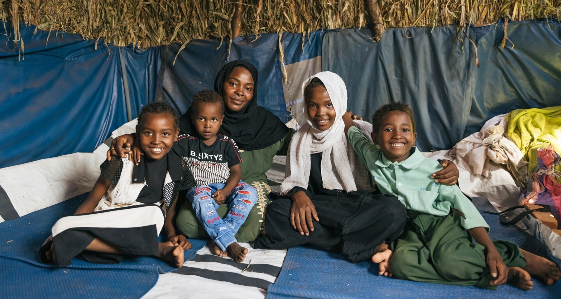 En mor og fire barn sitter i et telt og smiler.