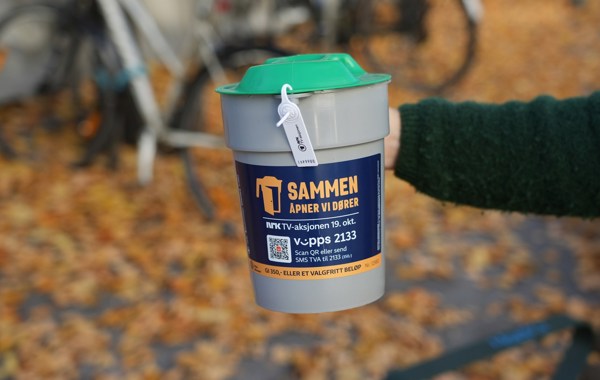 En hånd holder en grå bøsse med teksten Sammen åpner vi dører.
