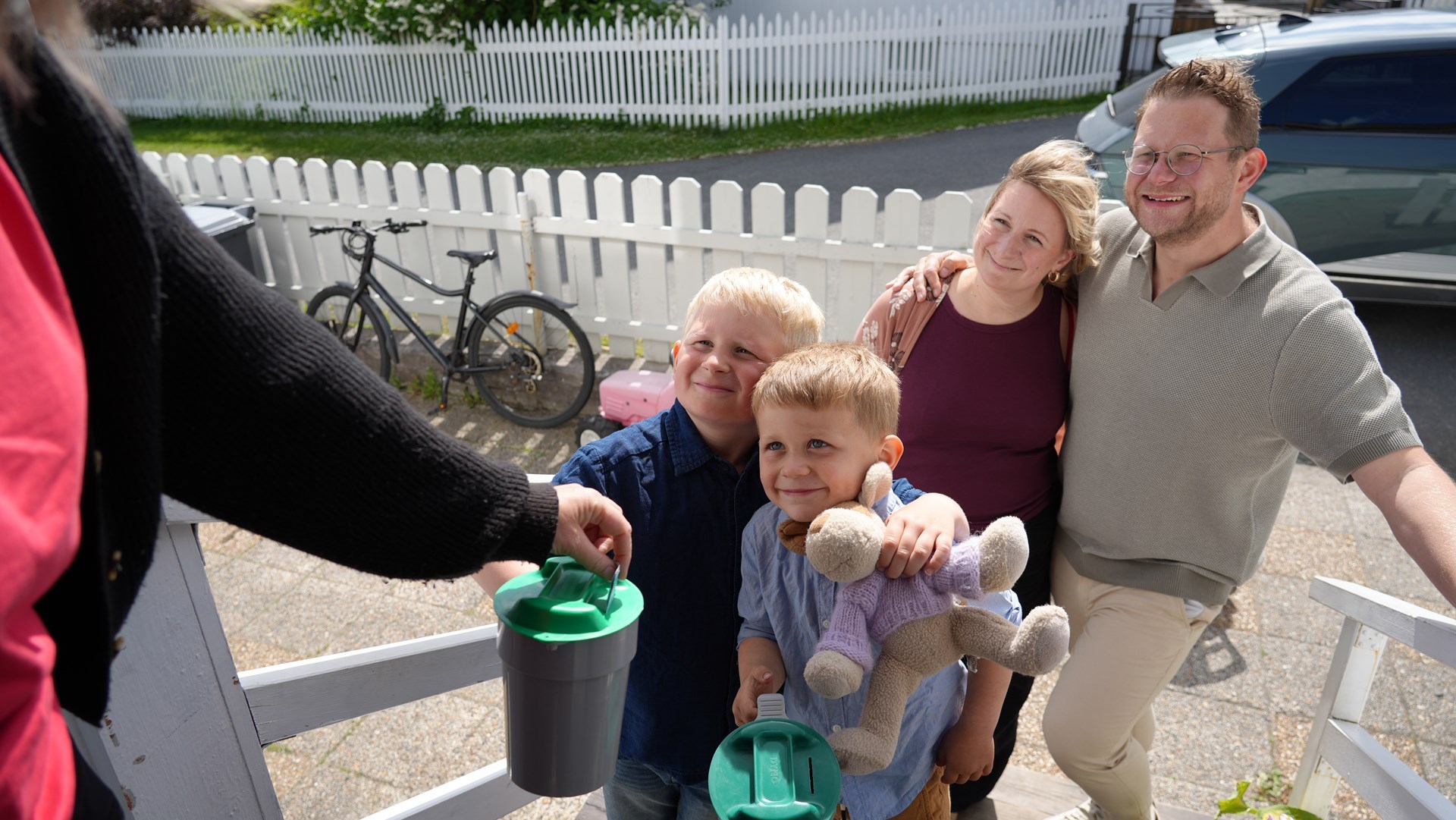 To voksne og to små gutter holder en bøsse. En dame gir penger på bøssa. 