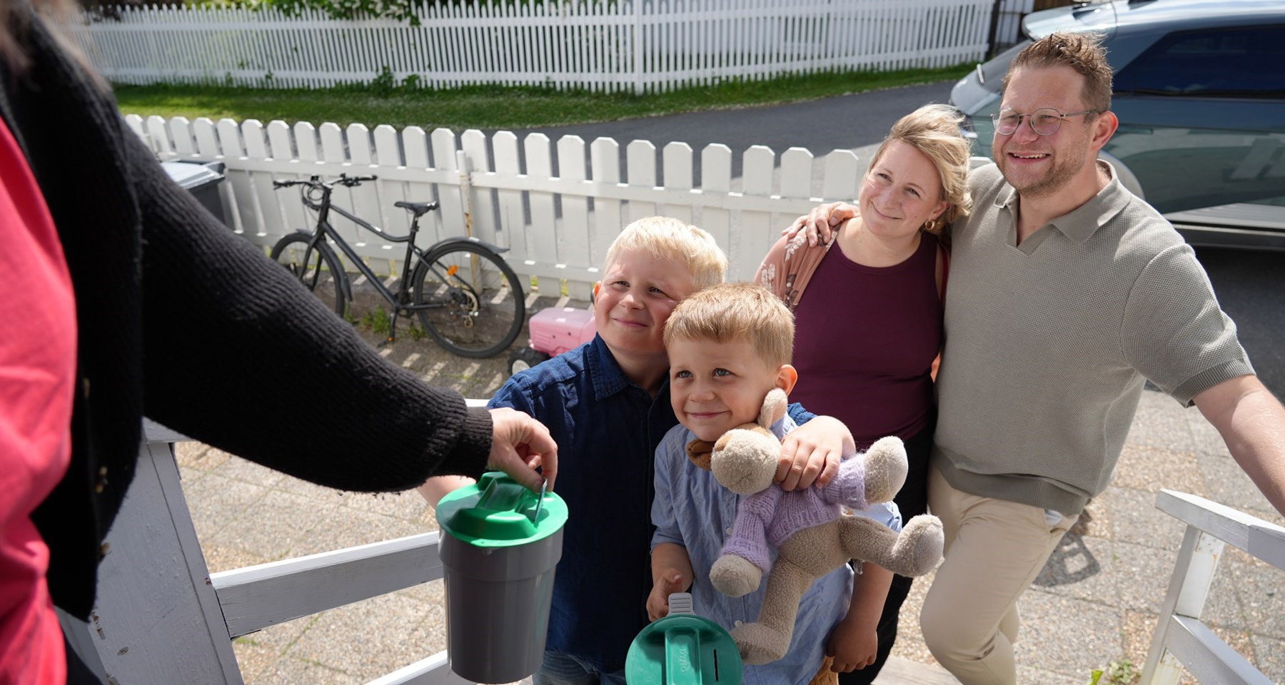 To voksne og to små gutter holder en bøsse. En dame gir penger på bøssa. 
