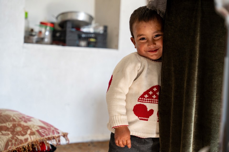 En liten gutt står inntil en grønn lang kjole og smiler. 