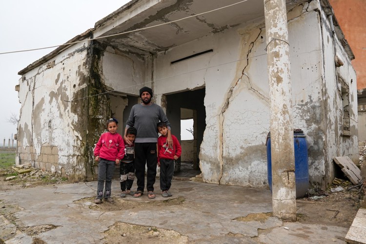 En mann og tre barn står ved et utbombet hus i Syria. 