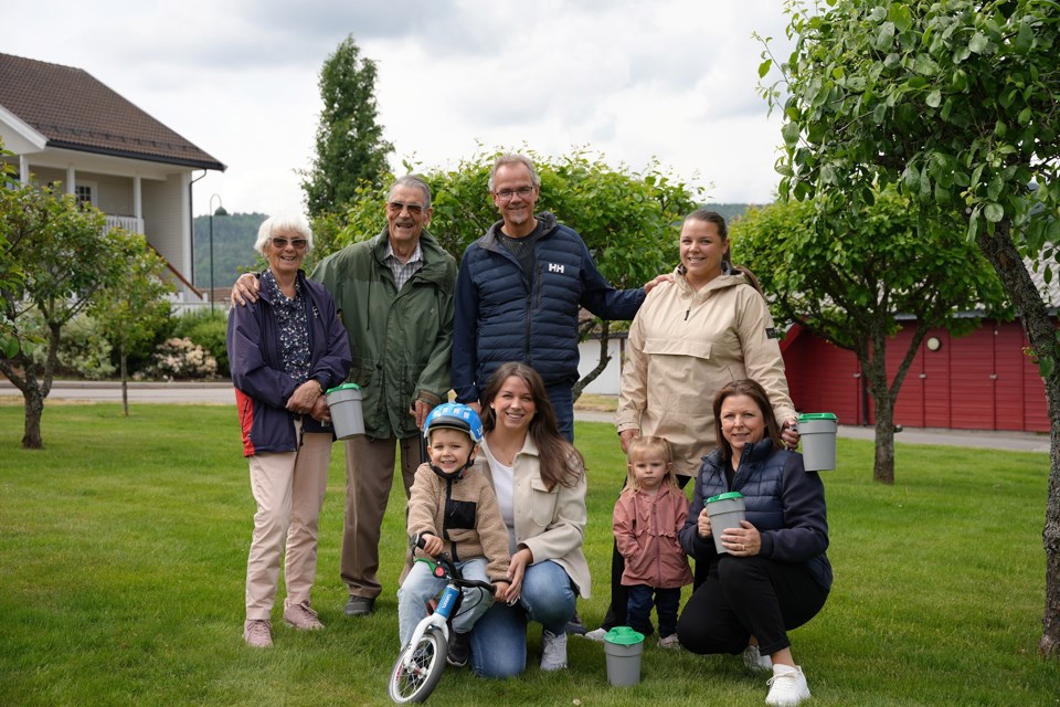 En familie med voksne og barn står i en hage med bøsser i hendene.