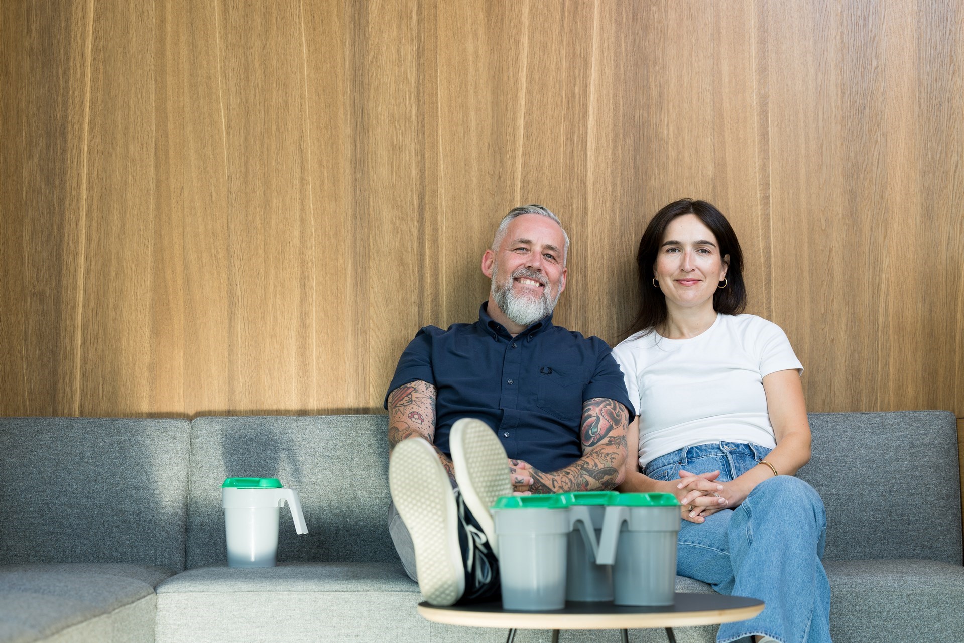 En mann og en kvinne sitter smilende i en sofa med bøsser på bordet foran. 