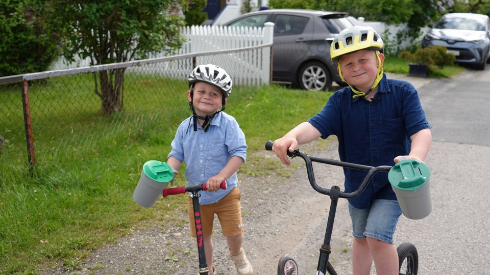 To små gutter har på hjelm og står på hver sin sparkesykkel med bøsse på styret. 
