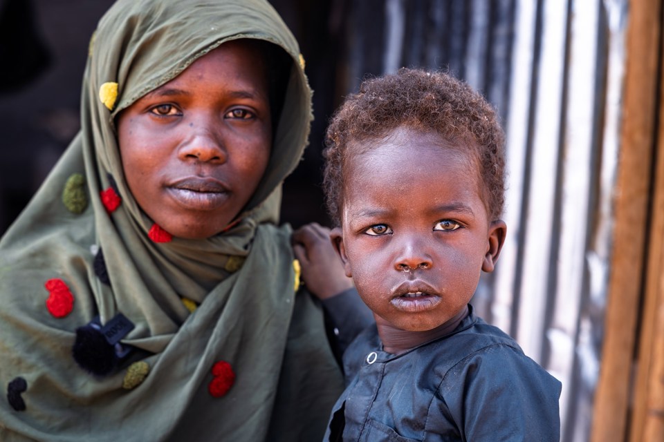 Kvinne med grønt sjal og liten gutt med blå skjorte ser inn i kamera. 