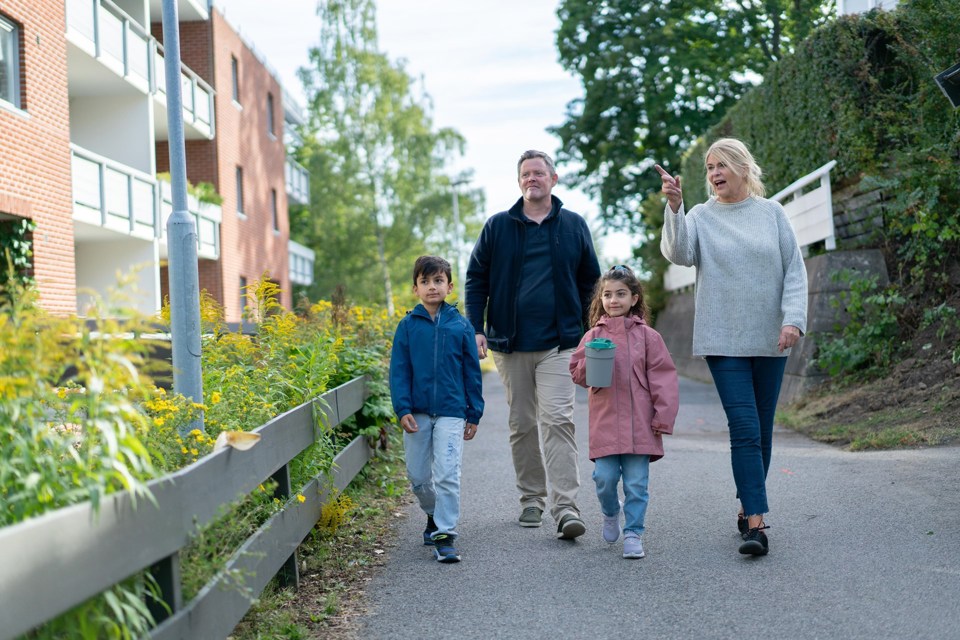 To voksne og to barn går på en vei utenfor en boligblokk. Jenta har en bøsse i hånda.